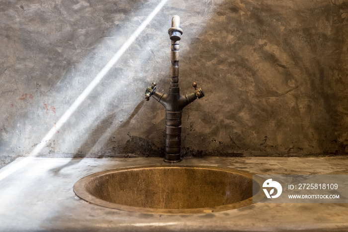 Luxury faucet with golden sink on the raw concrete counter in vintage bathroom. Line of sunlight hit