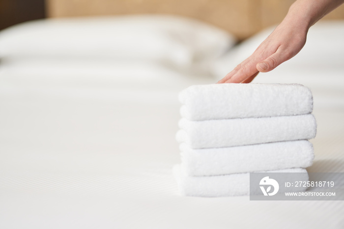 Female hand touching stack of fresh white bath towels on the bed