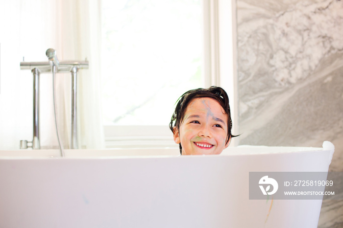 Boy (6-7) with painted face sitting in bathtub