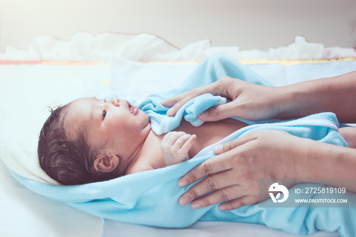 可爱的新生女婴沐浴后用毛巾与母亲双手温柔地擦干身体