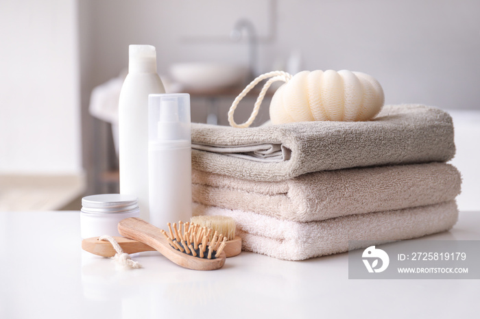 Stack of towels, cosmetics, loofah and brushes on table in bathroom