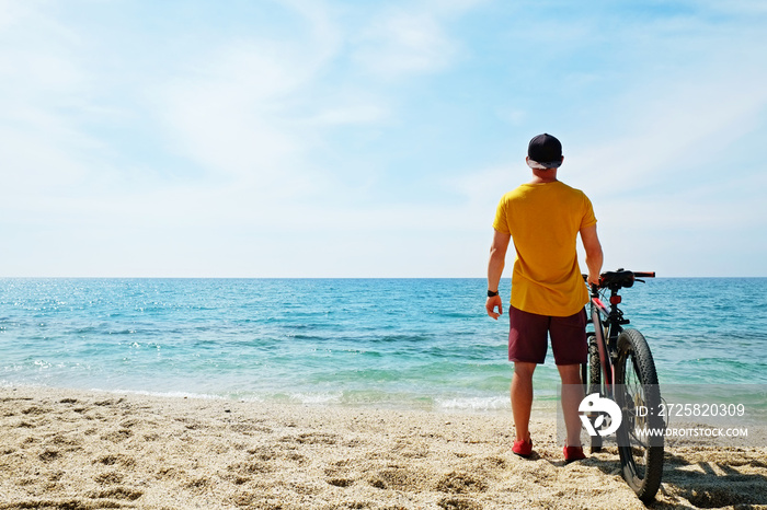 Young man with fit body riding the mtb mountain bike on sandy beach with beautiful azure water sea v