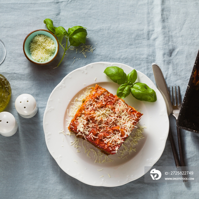 vegan lasagna with lentils and green peas in a baking sheet on a table with a blue linen tablecloth.