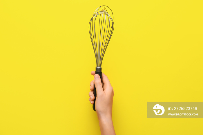 Female hand with whisk on color background