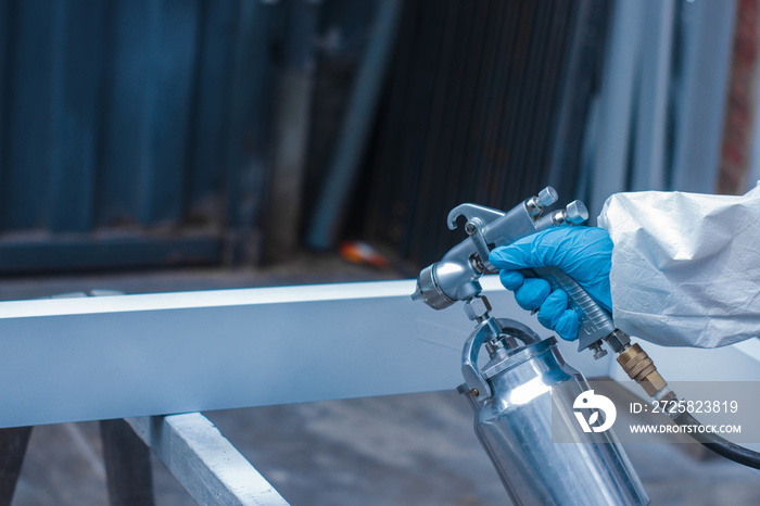 Closeup of a person wearing a protective suit and gloves spray painting in a workshop