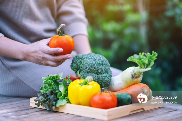 A woman holding and picking a fresh mixed vegetables from a wooden tray on the table