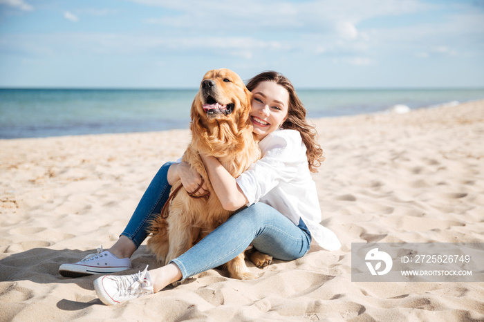 快乐的女人坐在海滩上拥抱她的狗