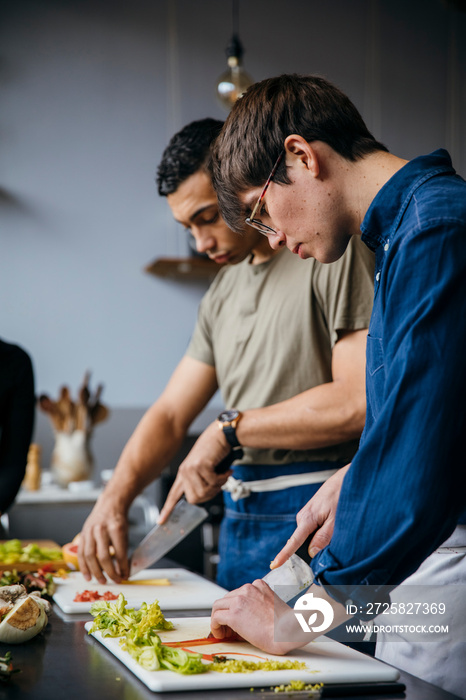 Male students chopping vegetables on table in training class