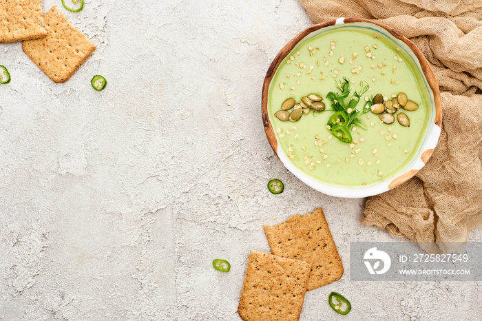 美味的绿色奶油汤俯视图，饼干，灰色纹理背景，质朴的布料