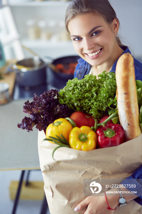 Young woman holding grocery shopping bag with vegetables .Standing in the kitchen