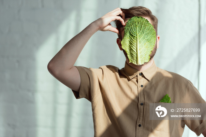 脸上长着萨沃伊卷心菜叶子的沉思男子的模糊视图，素食主义生活方式概念