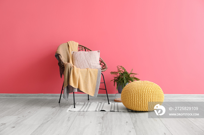 Pouf, houseplant, armchair with plaid and pillow near color wall in room