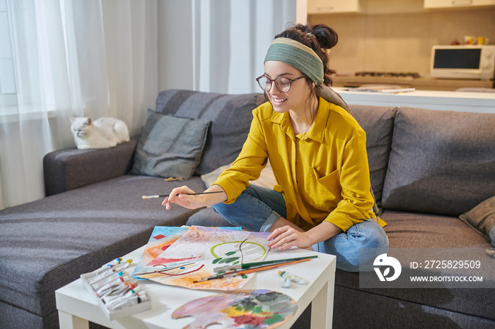 A woman in yellow shirt painting and looking involved