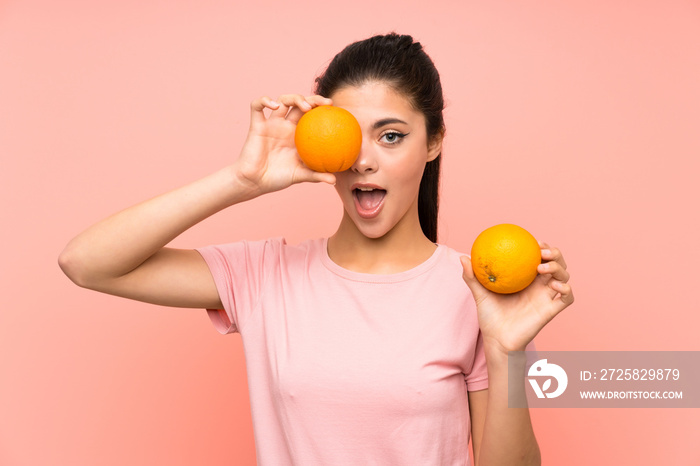 Happy Teenager girl  over isolated pink wall holding oranges