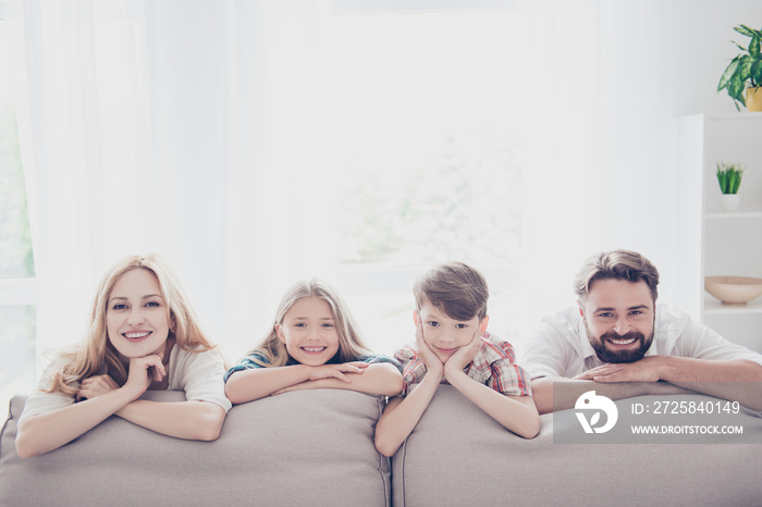 Happy parents and thier cheerful kids - blond small girl, brunet boy, lying on the beige sofa in a r