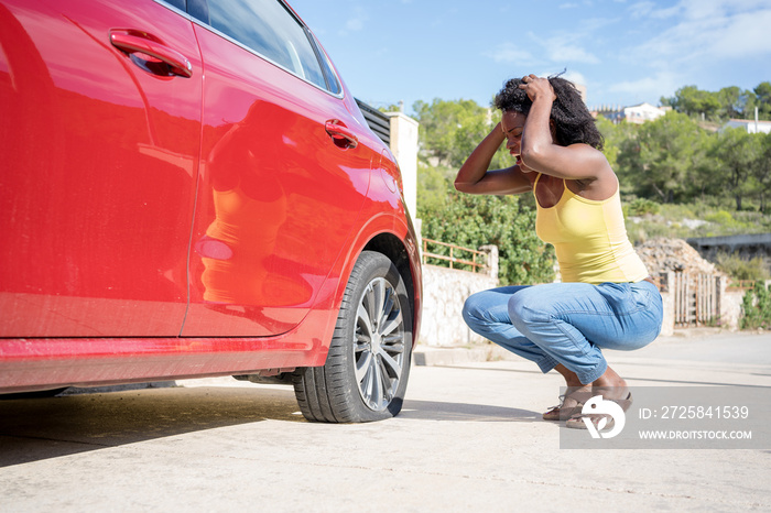 一名非洲妇女发现自己的红色汽车爆胎，非常担心
