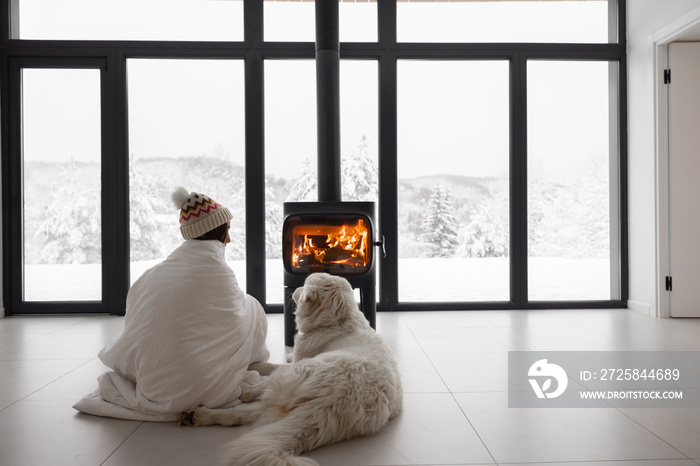 Woman sitting with her dog by the fireplace at modern house on nature during winter time. Concept of