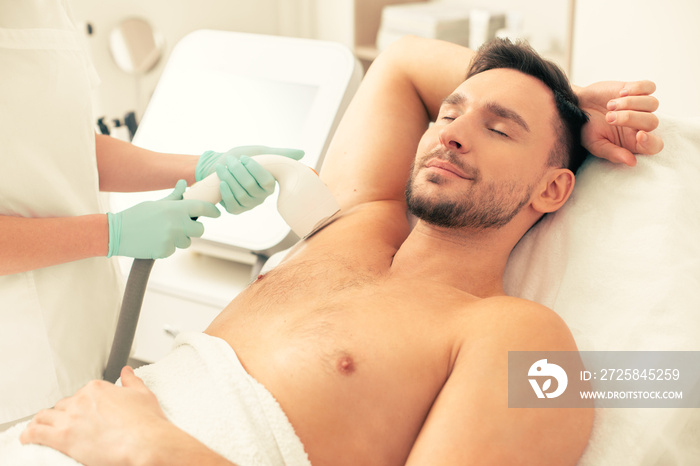 Smiling man undergoing laser hair removal in the clinic