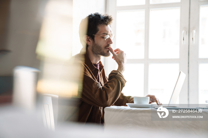 Image of handsome serious man using laptop while sitting