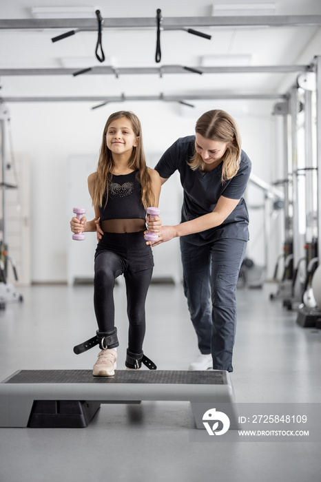 康复专家帮助小女孩在健身房锻炼。物理治疗的概念