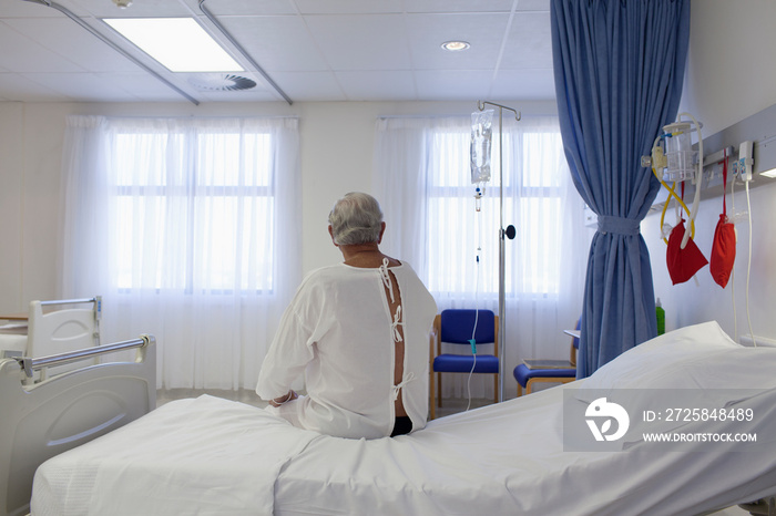 Worried male senior patient sitting on edge of hospital bed