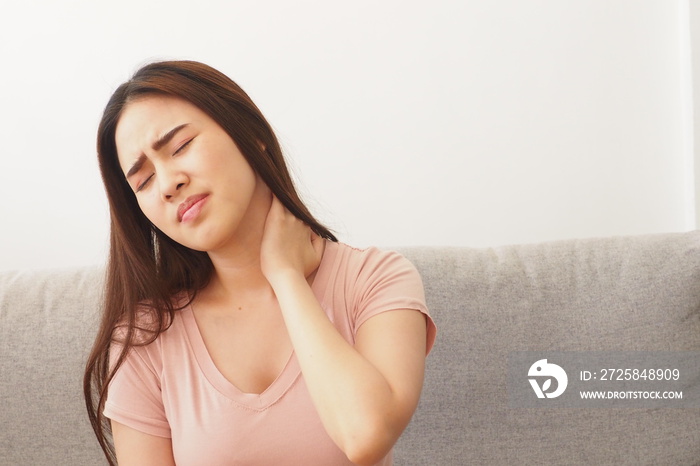 Young Asian woman touching her neck having neck pain at home caused by sitting in poor position when