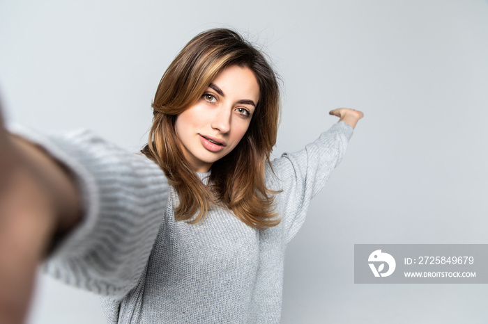 Portrait of a young attractive woman making selfie photo on smartphone isolated on a gray background