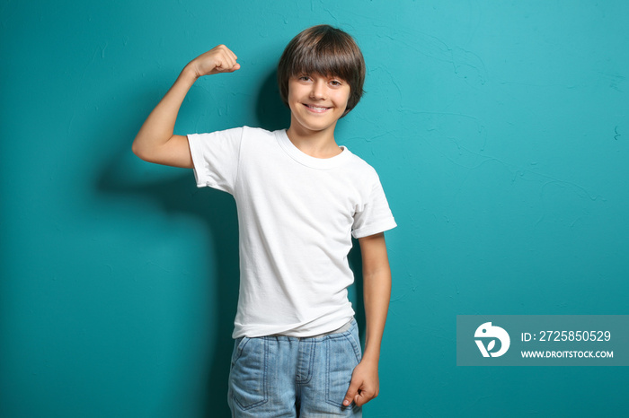 Little boy in t-shirt showing muscles on color background