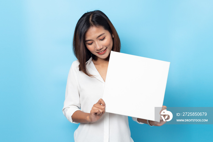 Portrait of young woman holding Empty white canvas frame for text or ad. isolated on blue background