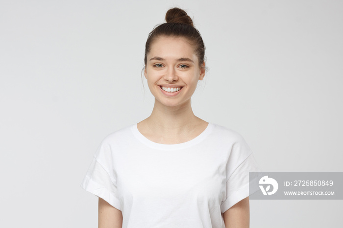 一位身穿白色t恤、面带微笑的年轻女子的特写照片，她看着镜头，被隔离在灰色的背上。