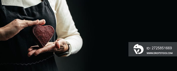 Female hands holding Red Heart shaped hard cheese on a dark background. Long banner format