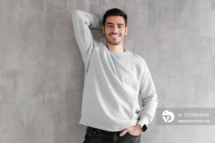 Hotizontal portrait of young man wearing gray sweatshirt, posing against textured wall