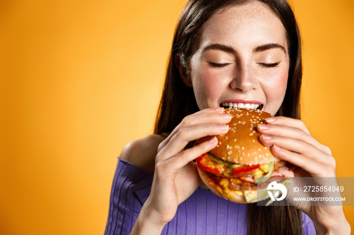 女孩满意地吃着芝士汉堡。女人开心地笑着吃着美味的汉堡。