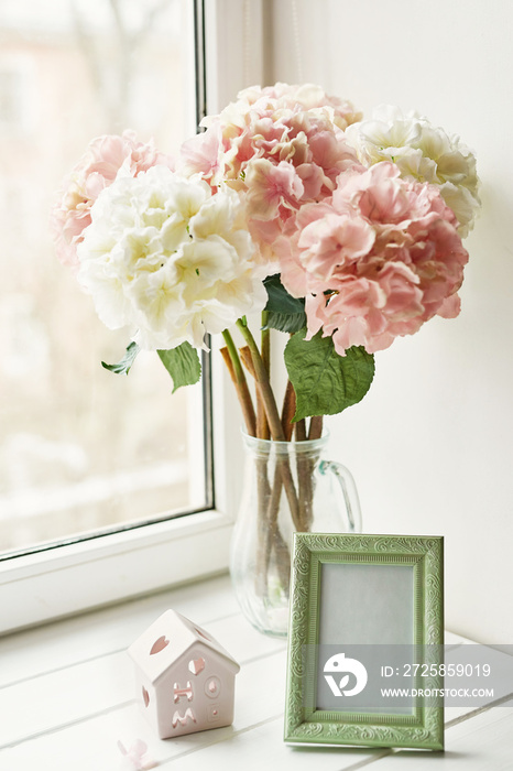 Light pink hydrangea for wedding bouquet in glass vase and photo frame on window background. Mother