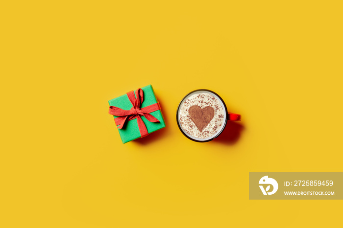 Holiday gift and cup of coffee with heart shape on yellow background.