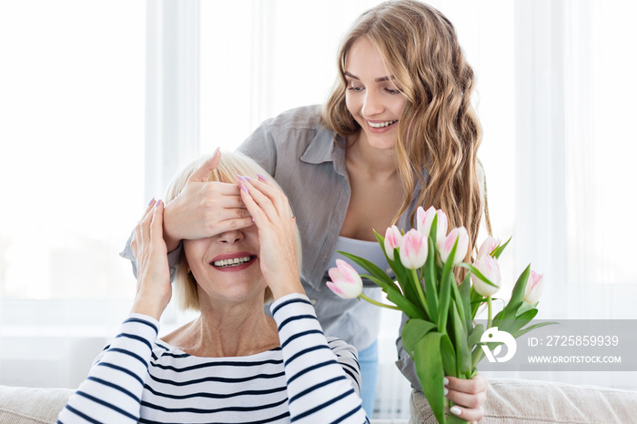 Woman holding bouquet and covering mothers eyes