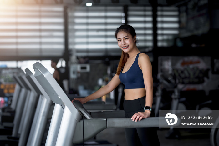 年轻的亚洲女性在健身俱乐部的机器跑步机上跑步。看着镜头。