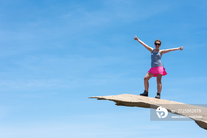 Brave young adult woman hiker stands on top of Potato Chip Rock in San Diego California