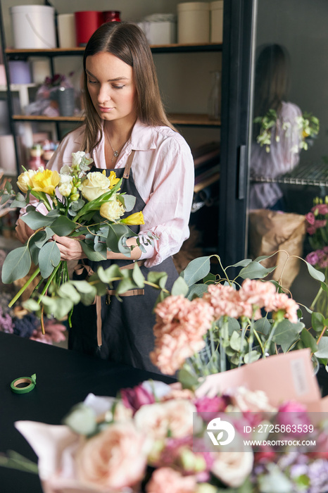 Photo of successful modern florist wearing apron making picture of flower, creating beautiful bouque