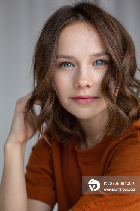 Portrait of white european young girl with short curly hair with blue eyes on grey