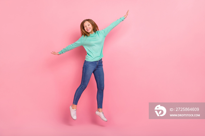 Photo of excited playful school girl dressed teal pullover arms sides jumping empty space isolated p