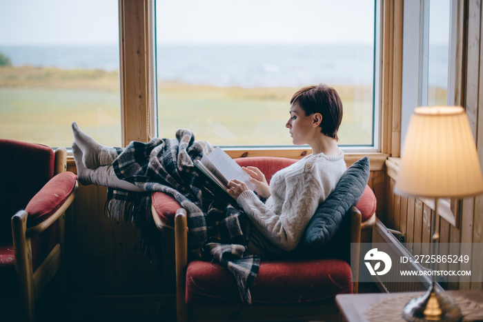 Young woman student reads a book at home on distance learning. Self isolation concept.