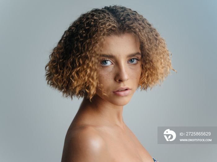 Portrait of a beautiful woman on a light background curly hair naked shoulders blue eyes