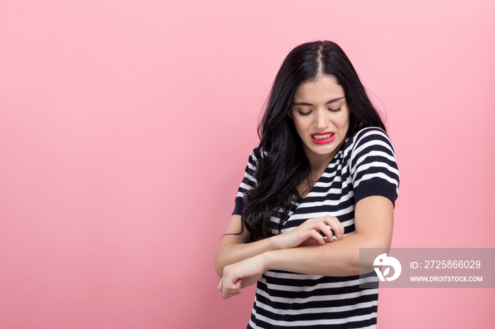 Young woman scratching her itchy arm on a pink background