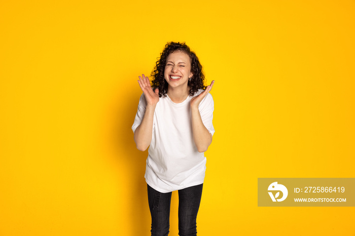 Portrait of smiling young beautiful girl in white t-shirt and jeans laughing isolated on yellow back