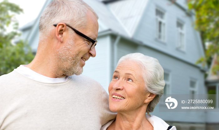 老年、住宿和房地产概念——幸福的老年夫妇在房子背景下拥抱