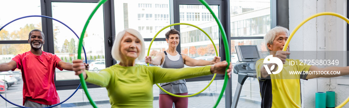 Smiling multicultural people exercising with hula hoops in gym, banner.