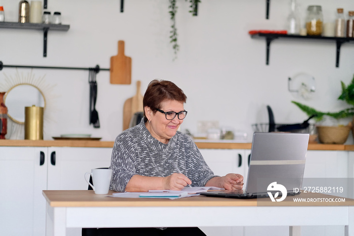 Senior woman using laptop for websurfing in her kitchen. The concept of senior employment, social se