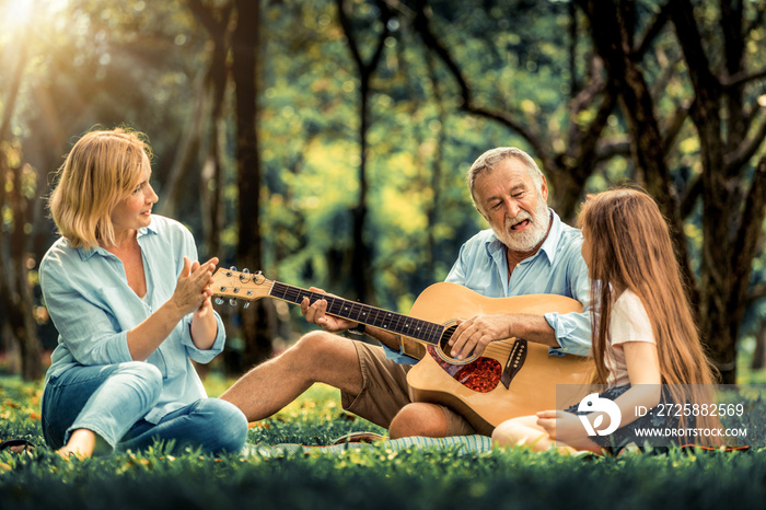 Happy family play guitar and sing together while sitting in the park in summer. Concept of family bo
