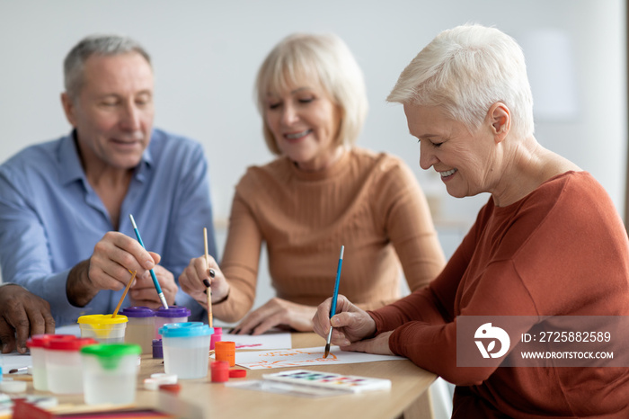 Positive elderly man and women enjoying painting with brush